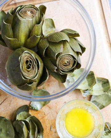 Fresh artichokes in a glass bowl with melted butter for dipping.