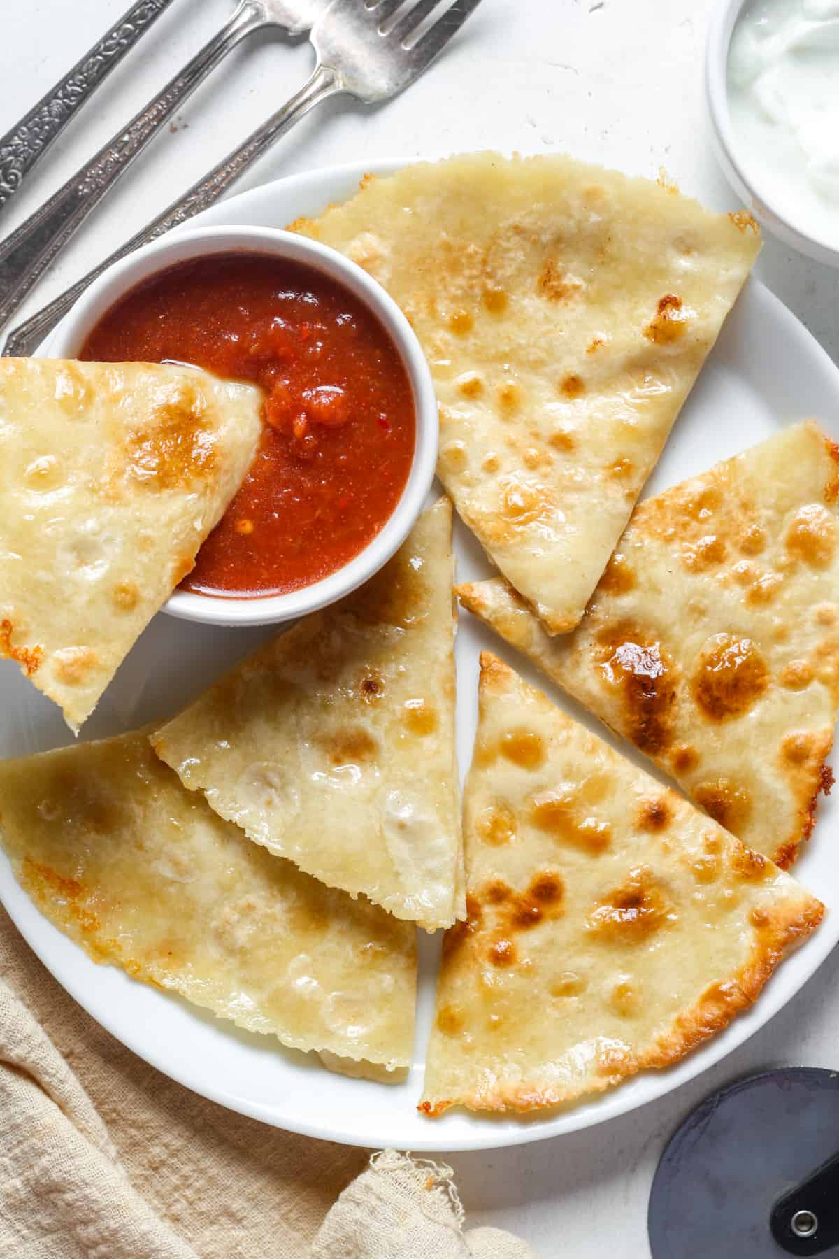 Cheese quesadilla triangles on a plate with a side of marinara sauce. 