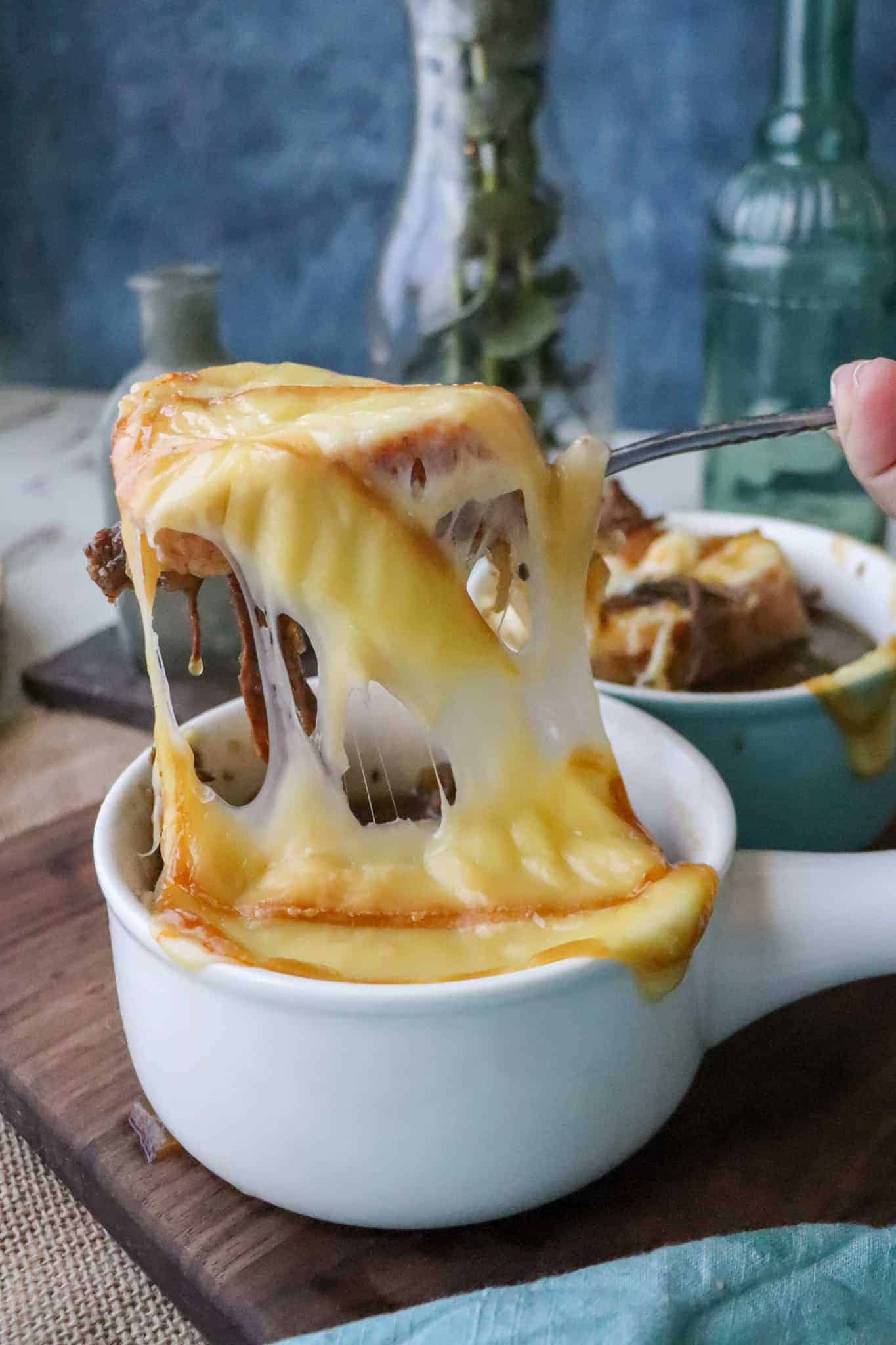 Bowl of beefy french soup with a melted cheesy pull coming up out of the bowl on a spoon. 