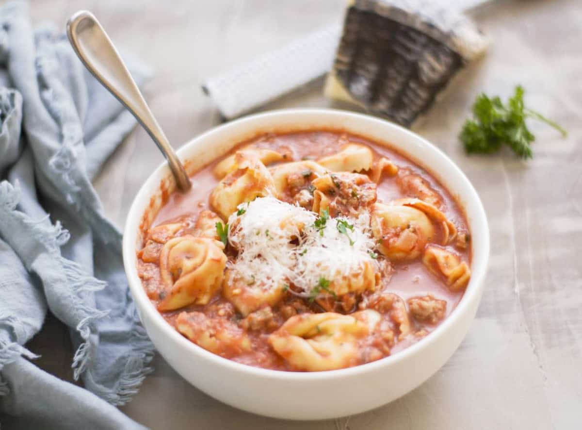 Spoon resting in a bowl of Italian tortellini soup. 