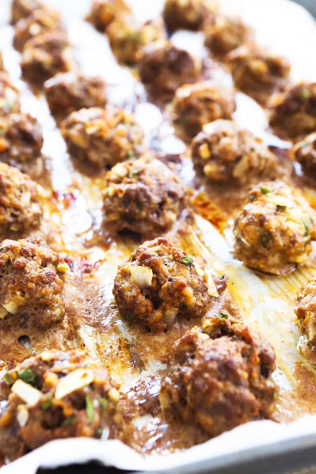 Baking sheet lined with parchment and topped with rows of cooked meatballs.