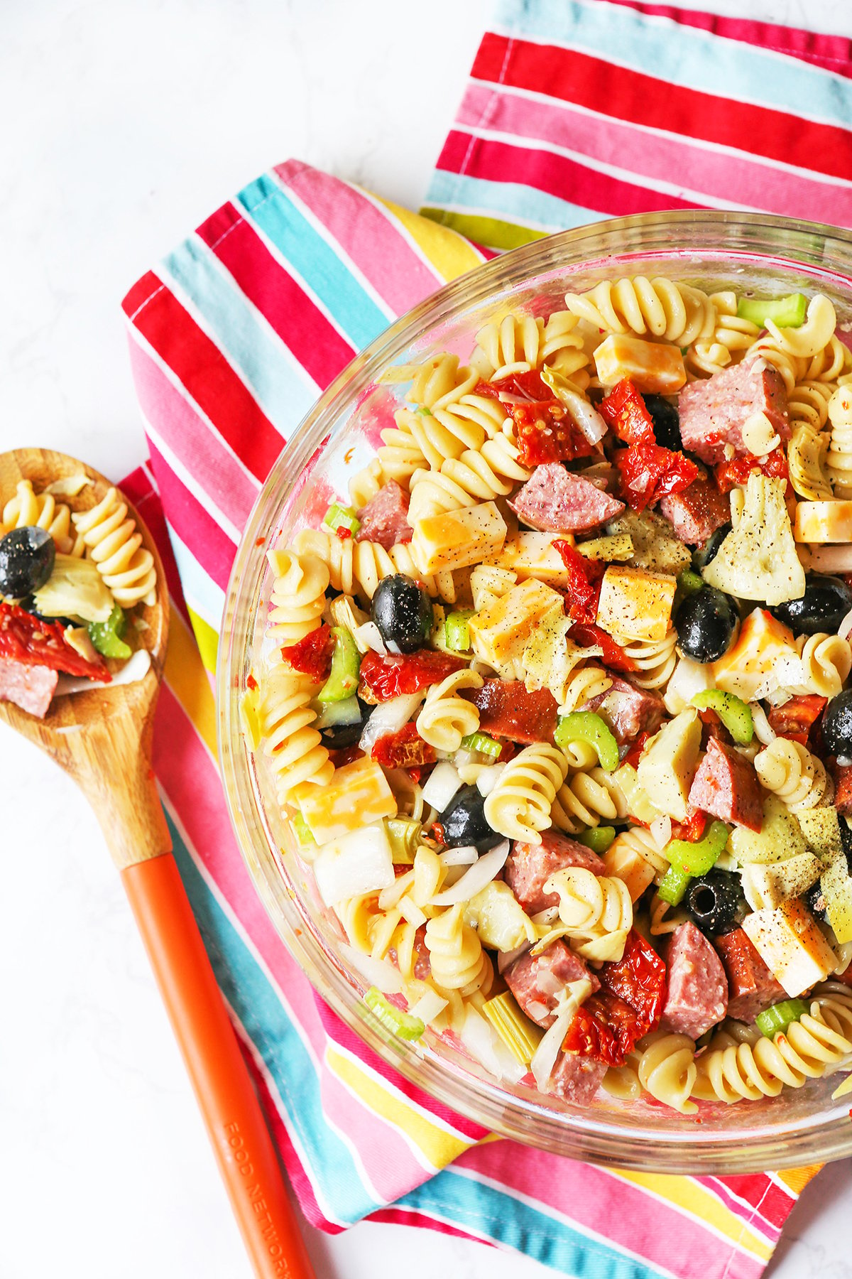 Top view of a bowl of pasta salad with a wooden spoon nearby.