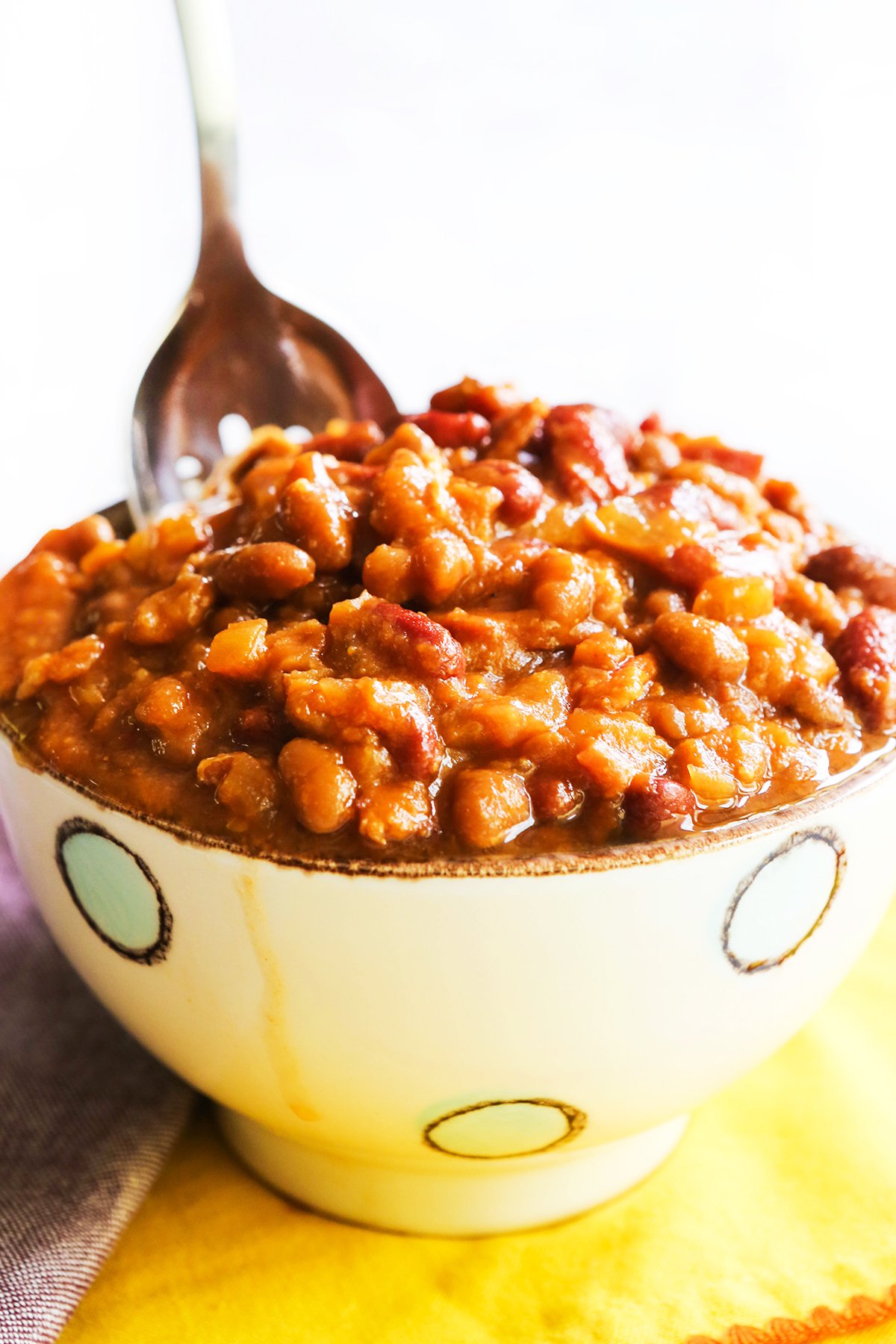 Serving spoon sticking out of a bowl filled with baked beans.