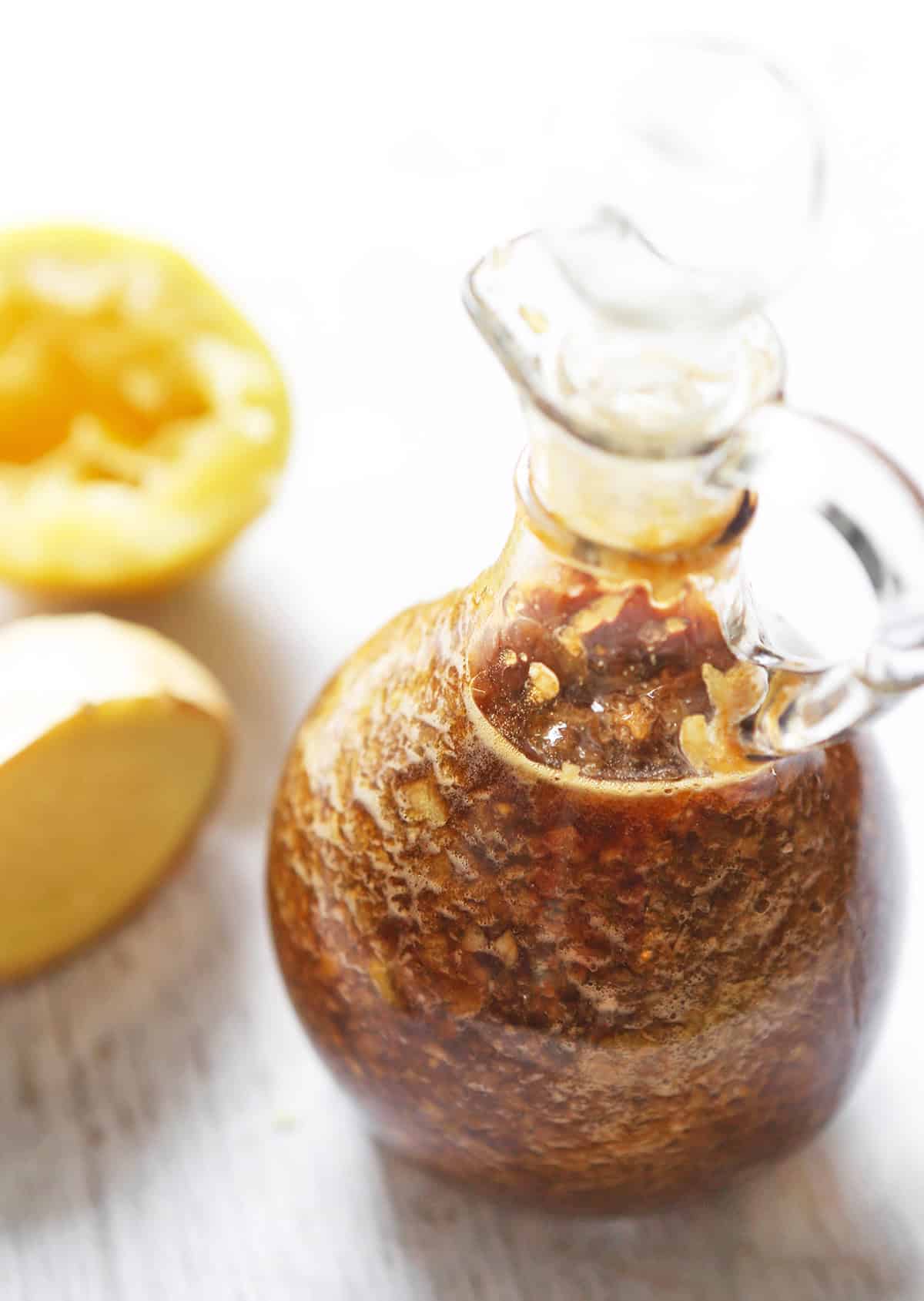 Glass bottle of lemon honey syrup with fresh lemon halves in the background.