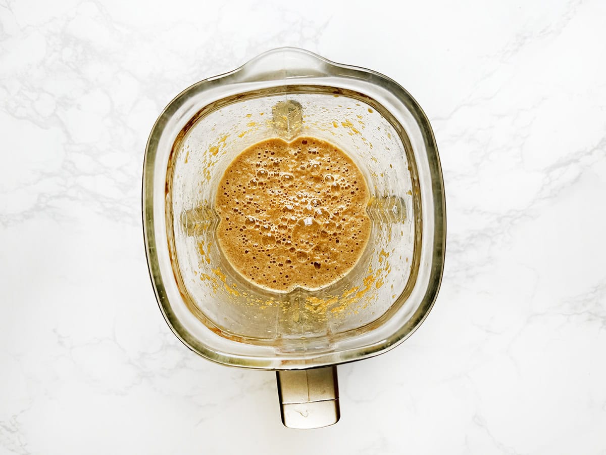 Creamy pumpkin spice smoothie blended in a glass blender on white marble background.