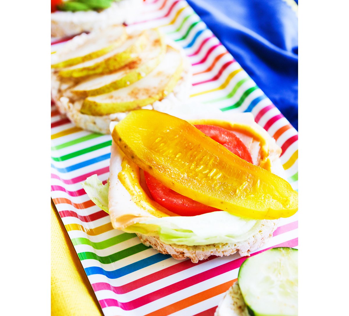 Rice cakes on a platter with different toppings such as turkey, tomato and pickles.