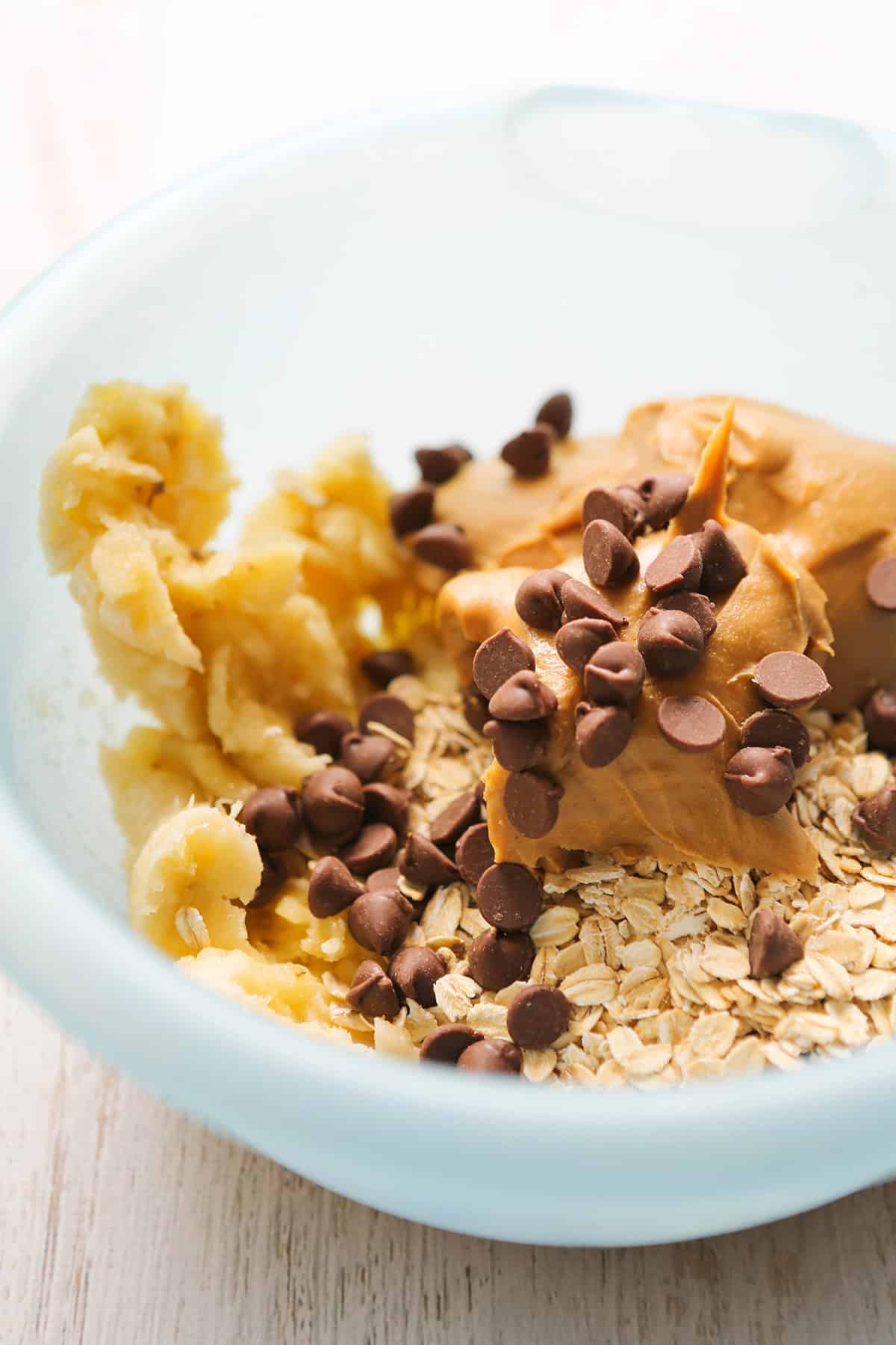 Close-up of peanut butter cookie dough with chocolate chips in a light blue bowl.