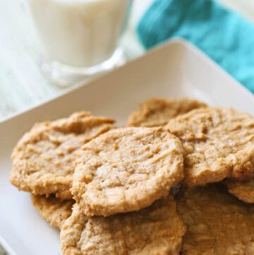 Homemade peanut butter cookies on a white plate with a glass of milk.