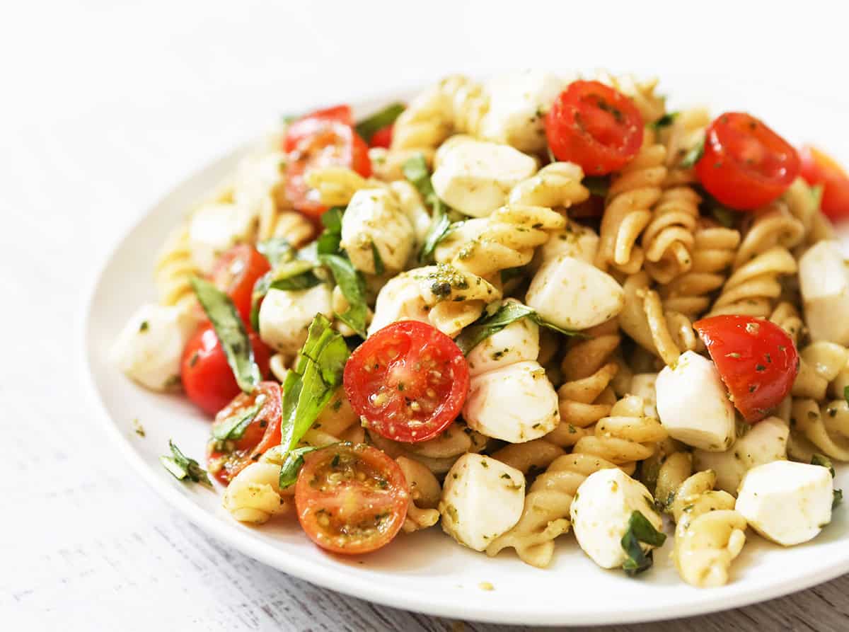 Pesto Caprese Pasta Salad with cherry tomatoes, mozzarella, and basil on a white plate.