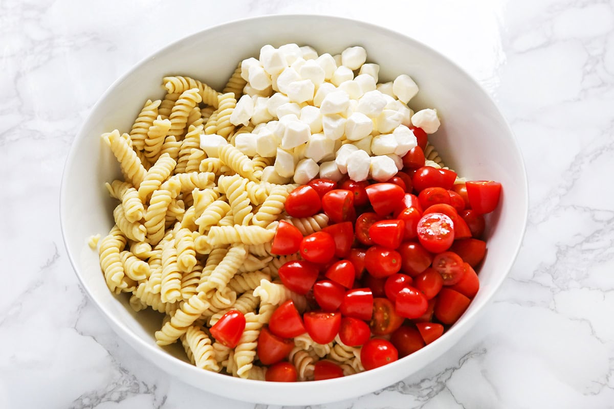 Fusilli pasta, cherry tomatoes, mozzarella balls in a white bowl.