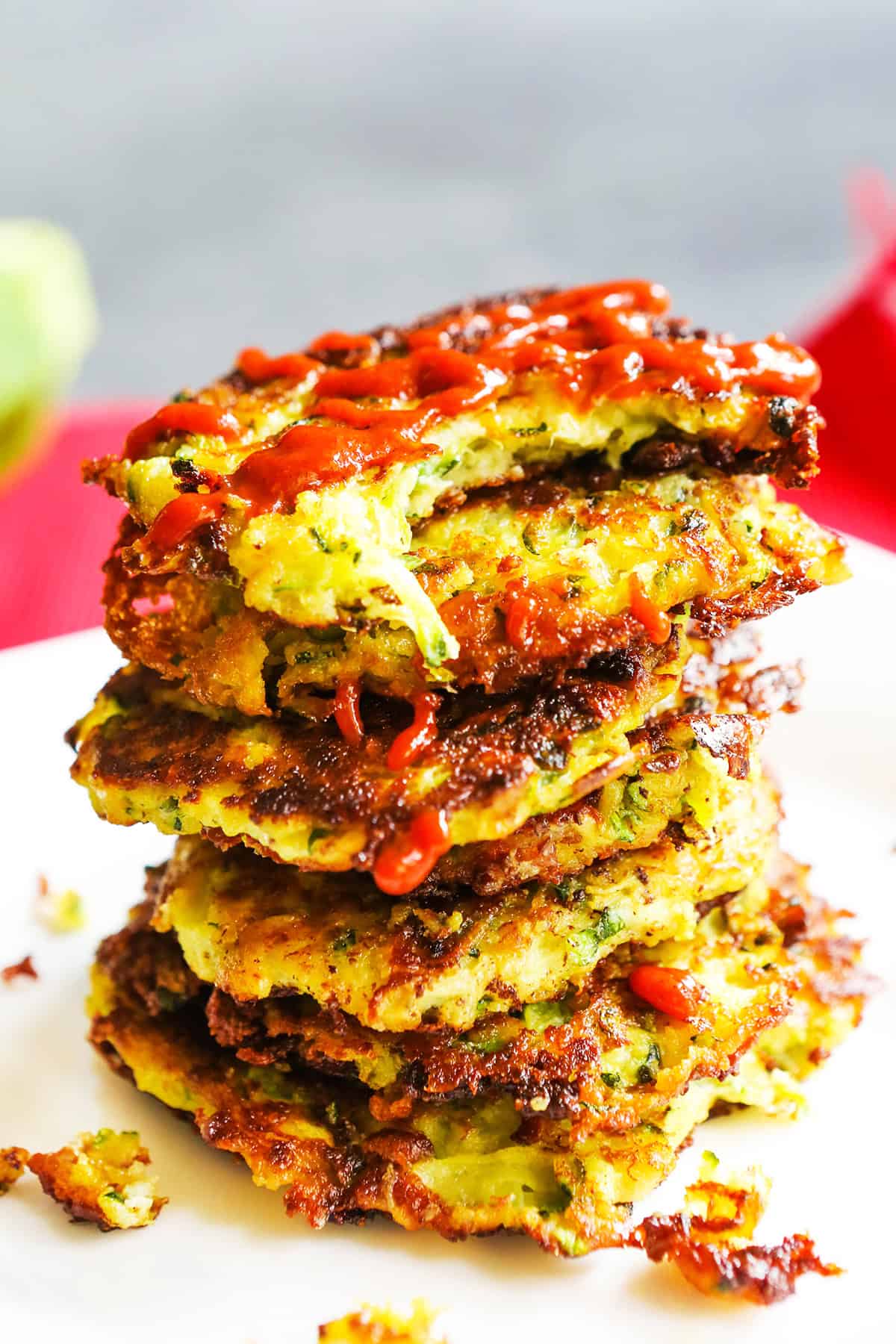 Close up stack of spicy zucchini fritters with sriracha sauce drizzled over the top.