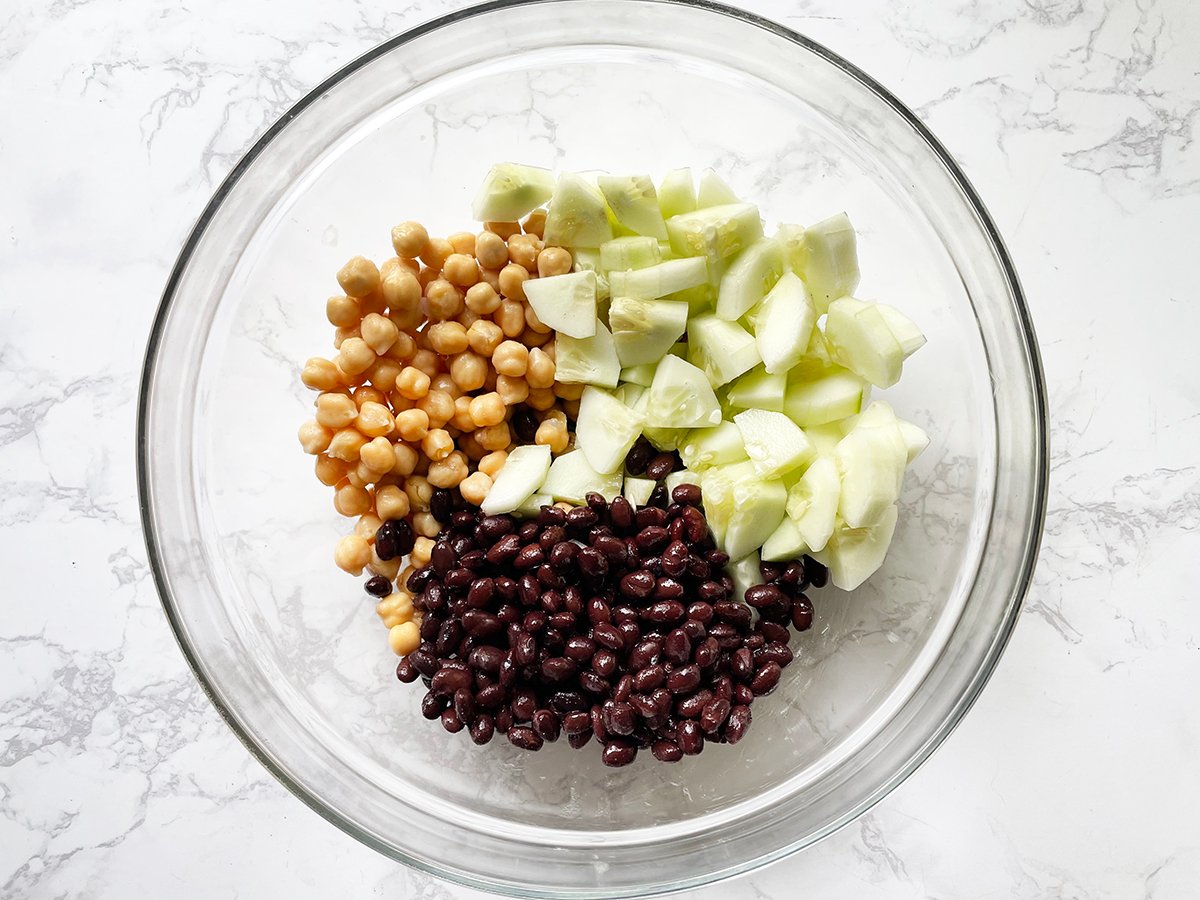 Chickpeas, black beans and cucumbers in a large glass mixing bowl.