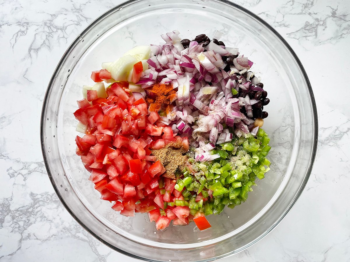Tomatoes, peppers, onions and seasonings in a glass mixing bowl.