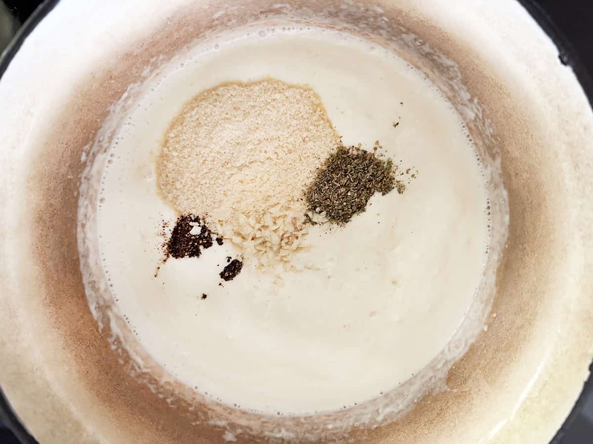 Looking down into a Dutch over filled with a creamy sauce, and with parmesan cheese and seasonings on top.