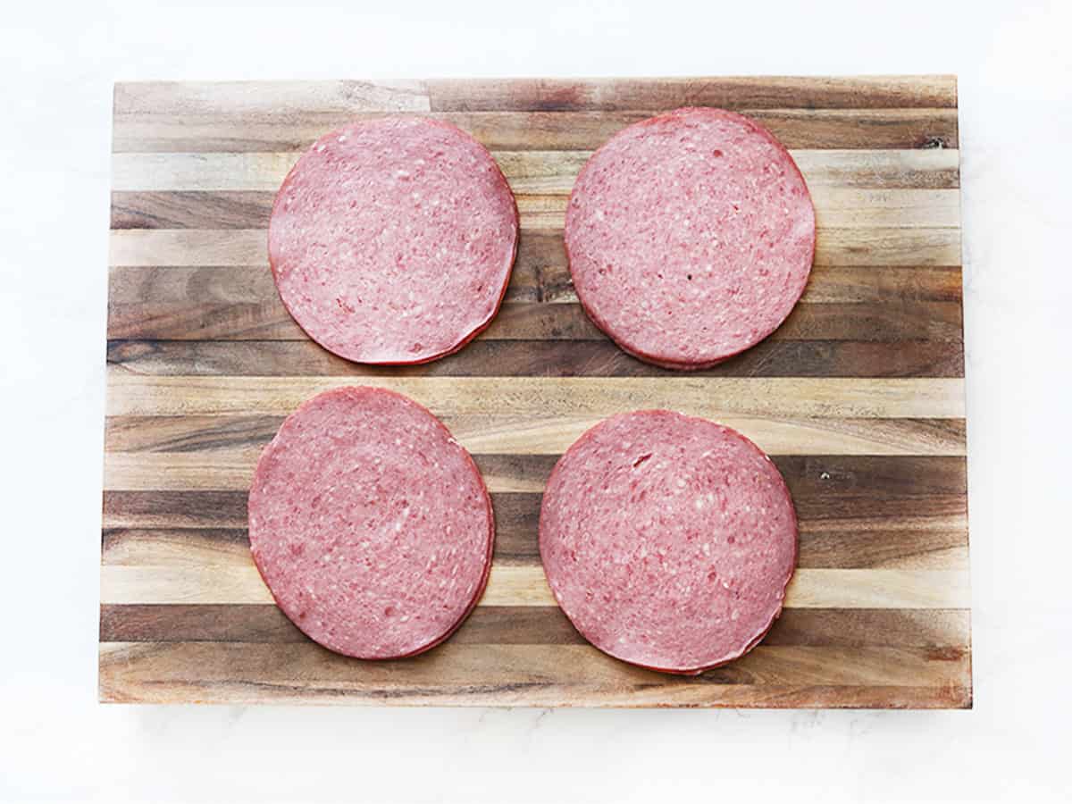 Four slices of deli meat on a wooden cutting board for appetizer.