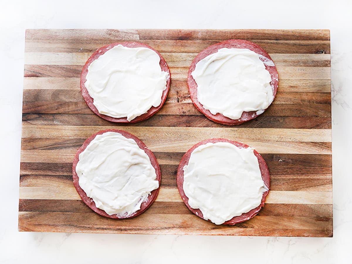 Four pickle roll ups with cream cheese on a wooden cutting board.
