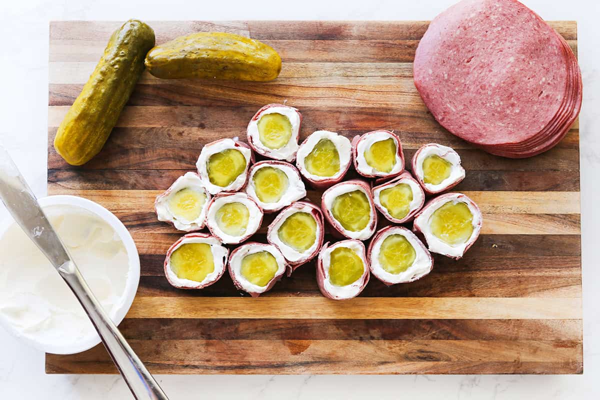 Pickle roll ups with cream cheese and ham on a wooden board.