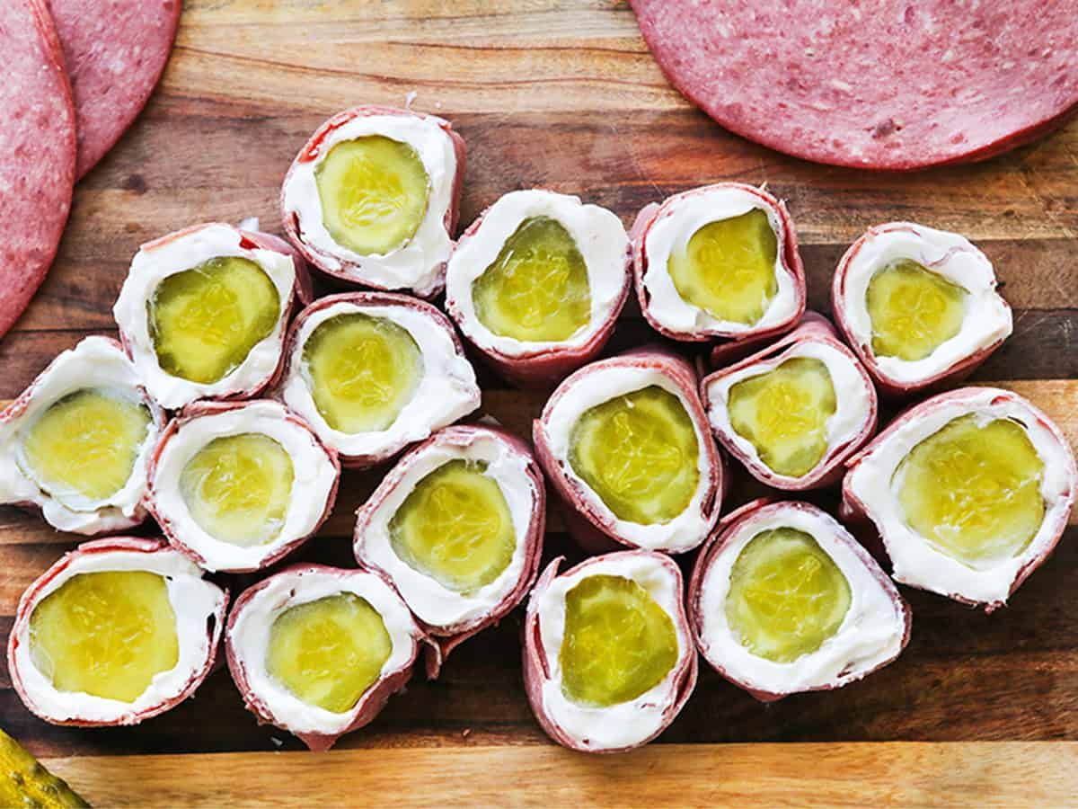 Pickle roll ups with cream cheese and ham on a wooden surface.