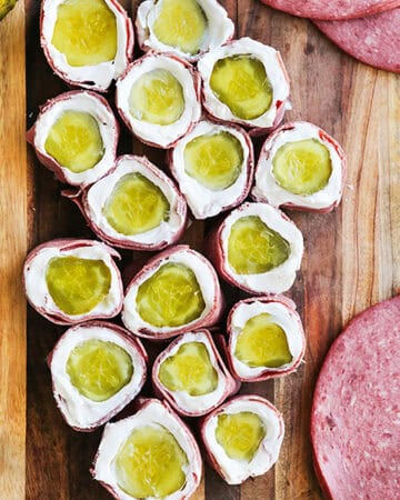Pickle roll ups with cream cheese and ham on a wooden board.