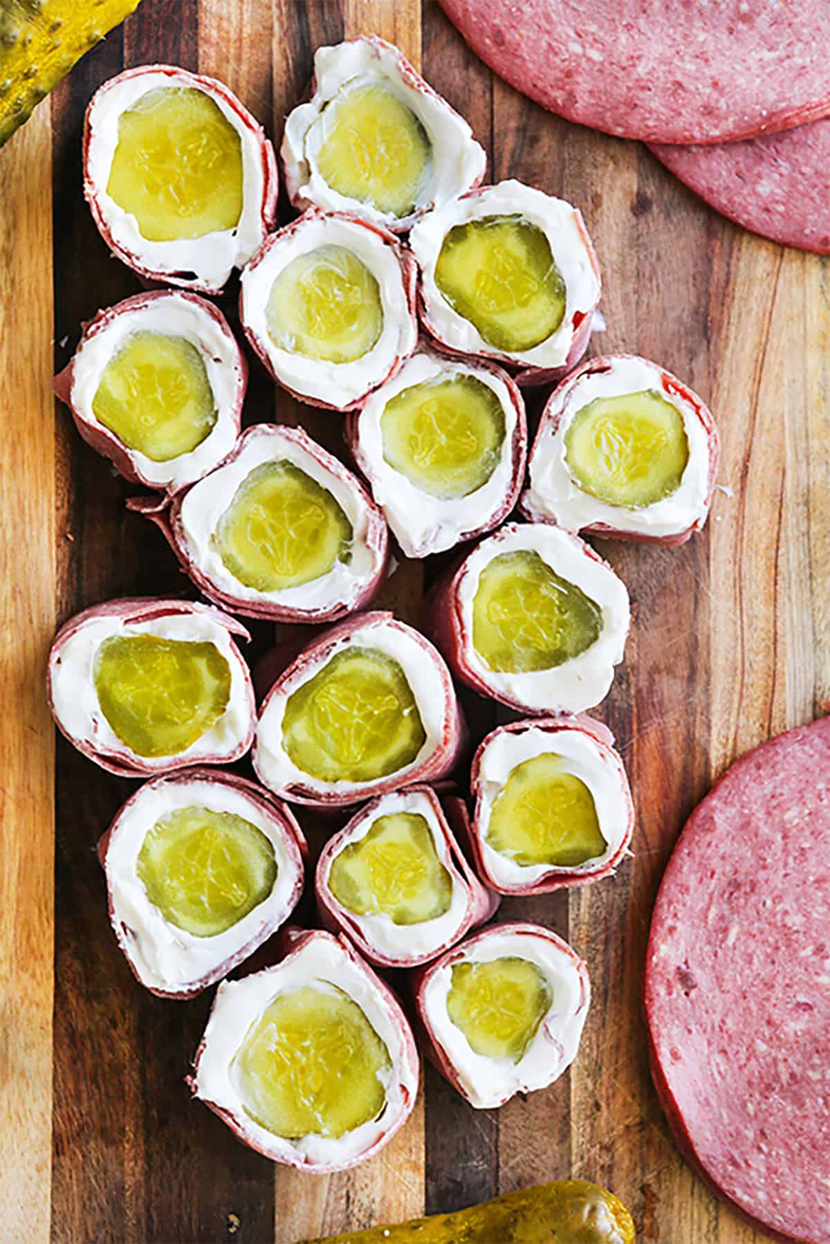 Pickle roll ups with cream cheese and ham on a wooden board.