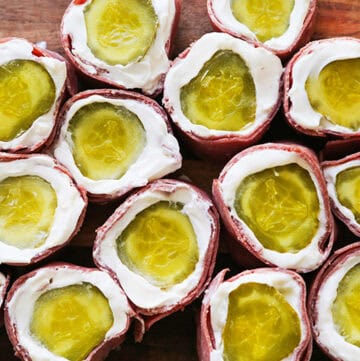 Pickle roll ups with cream cheese and ham on a wooden surface.