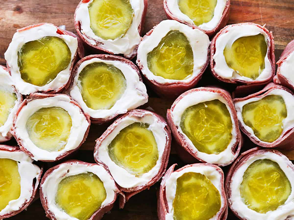 Pickle roll ups with cream cheese and ham on a wooden surface.
