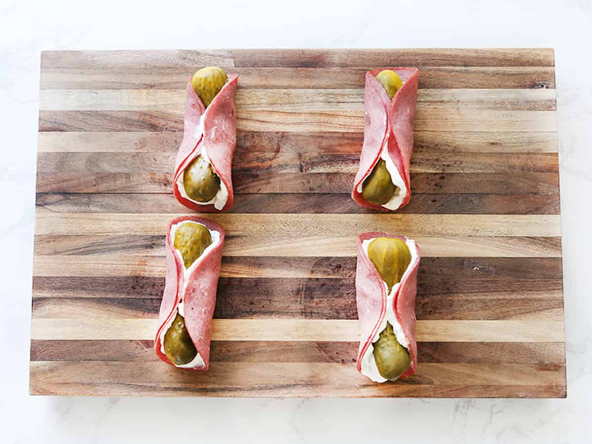 Four pickle roll ups with ham and pickles on a wooden board.