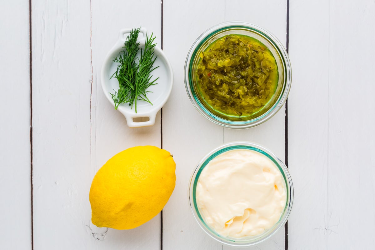 Dill, relish, a lemon and mayo on a white wood table.