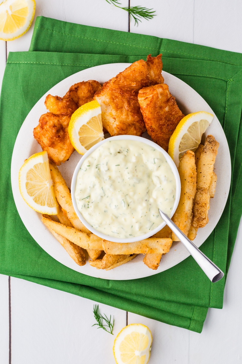Looking down on a plate of fish sticks, fries and a bowl of tartar sauce.