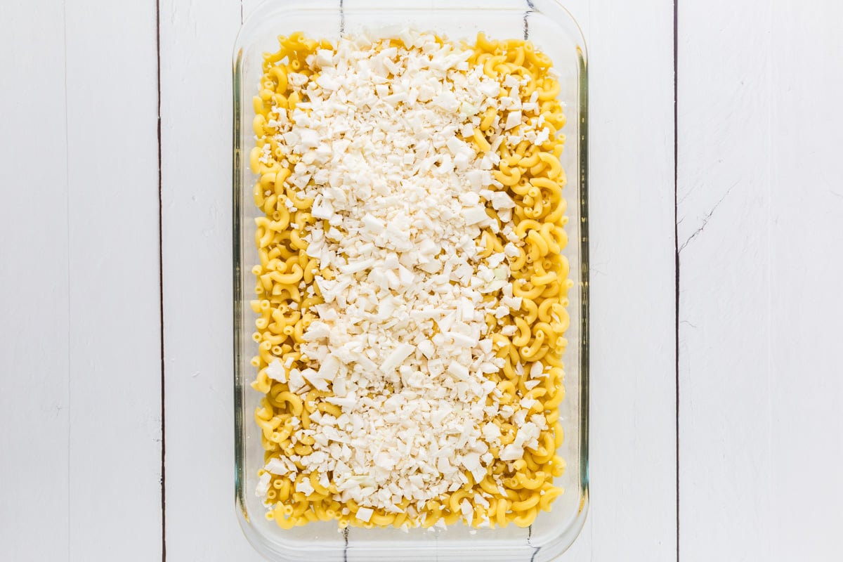 Glass baking dish filled with cooked pasta and a layer of chopped cauliflower.