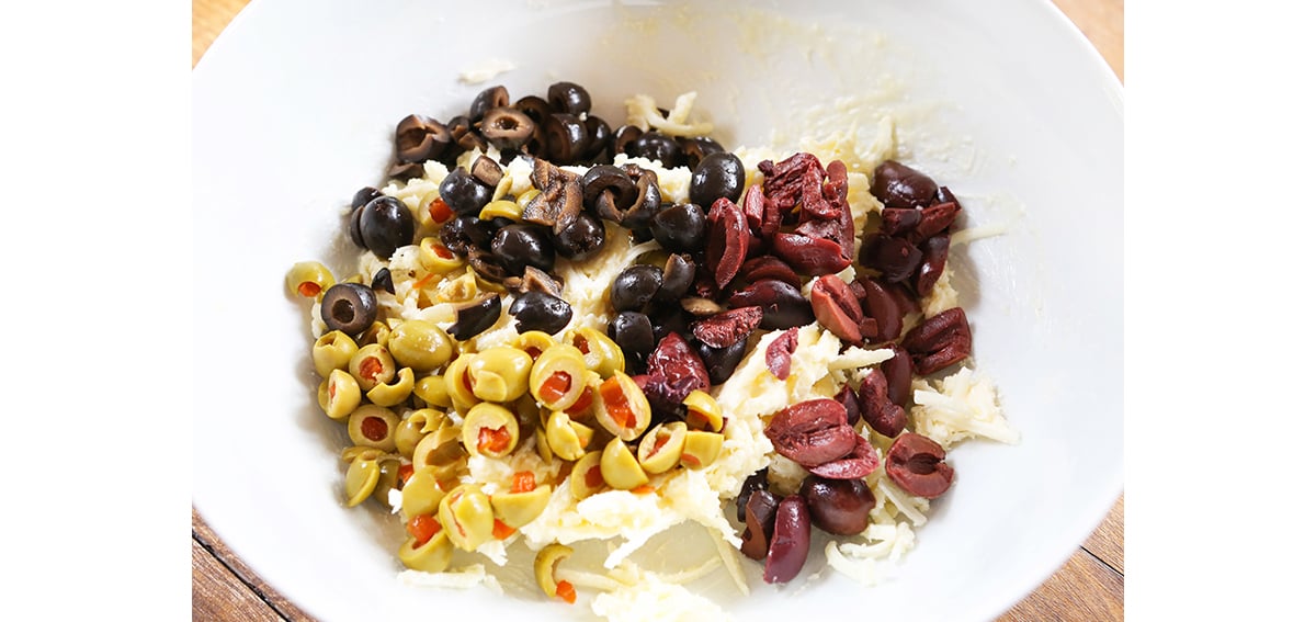 Variety of chopped olives in a mixing bowl, along with shredded mozzarella cheese.