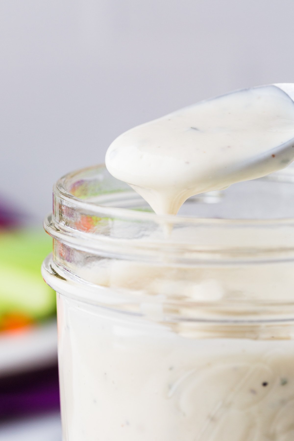 Spoon with ranch dressing in it hovering over a mason jar filled with more dressing.