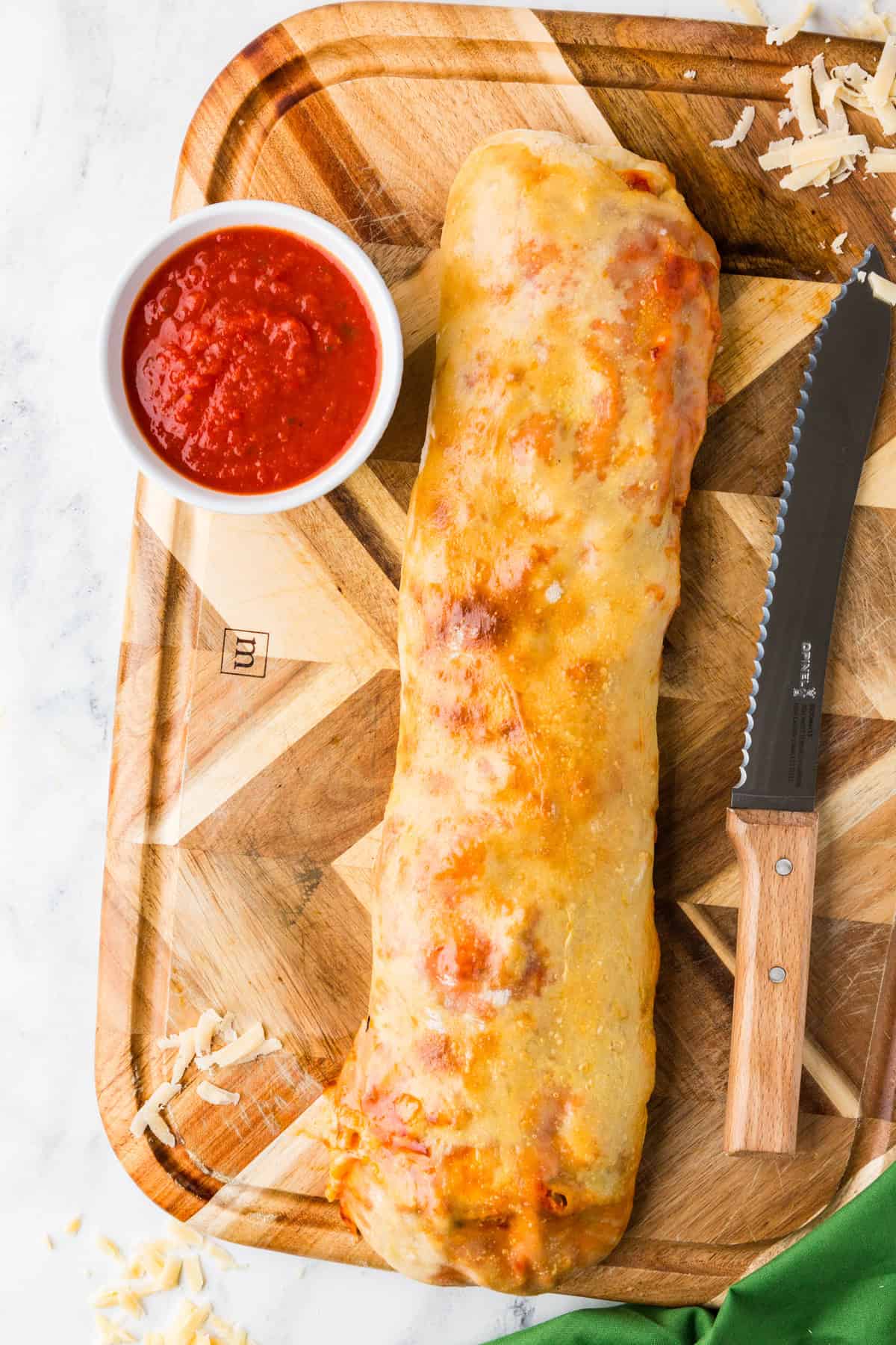 Stromboli log after baking and before slicing, on a cutting board with marinara.