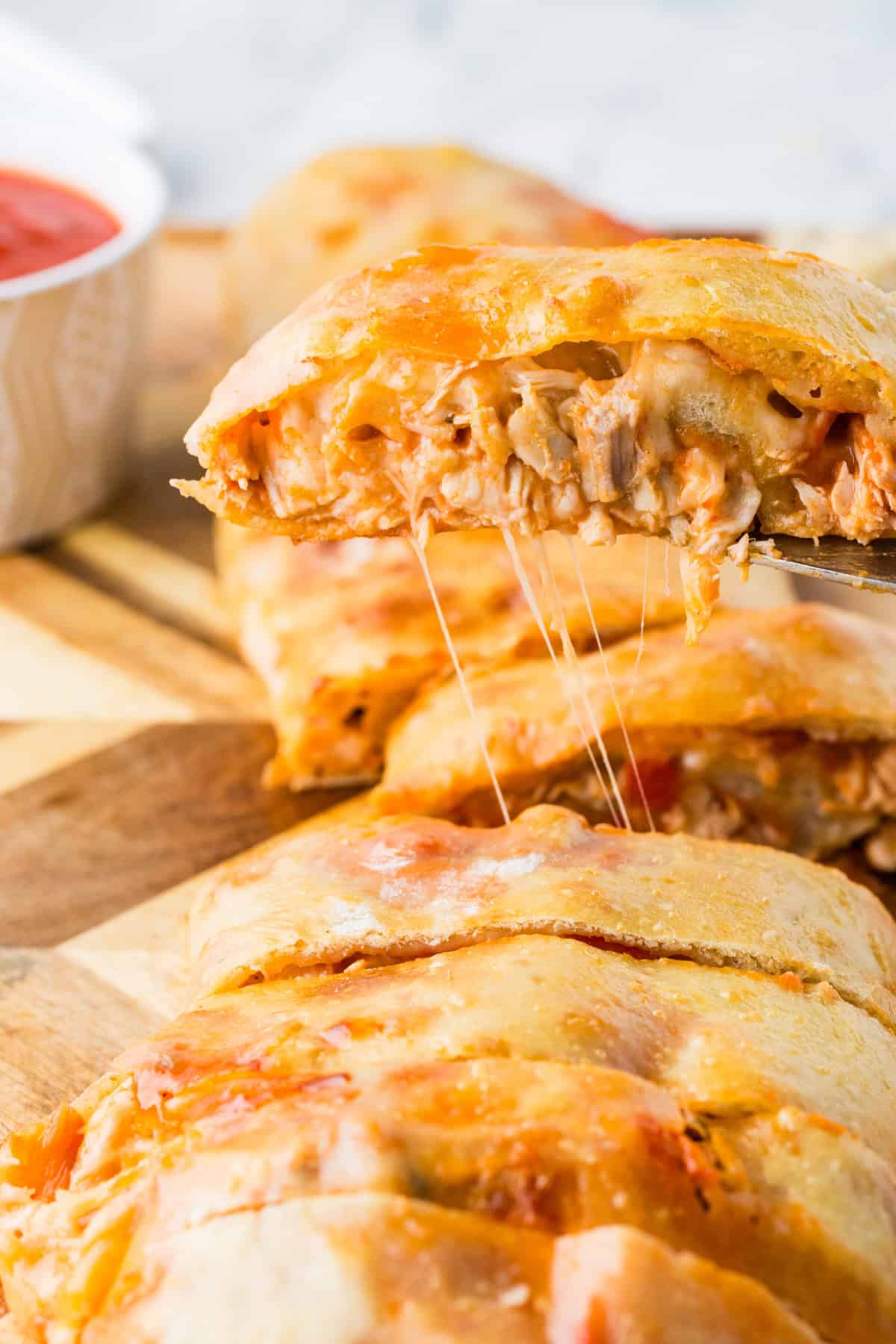 Piece of stromboli being pulled up away from the rest of the roll, on a spatula.