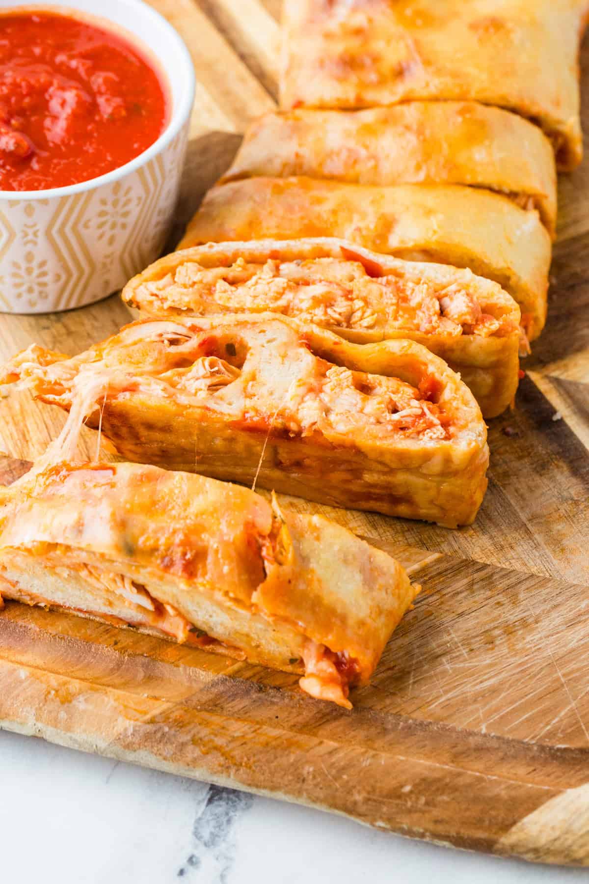 Chicken stromboli cut into slices on a cutting board, next to a small bowl of marinara.