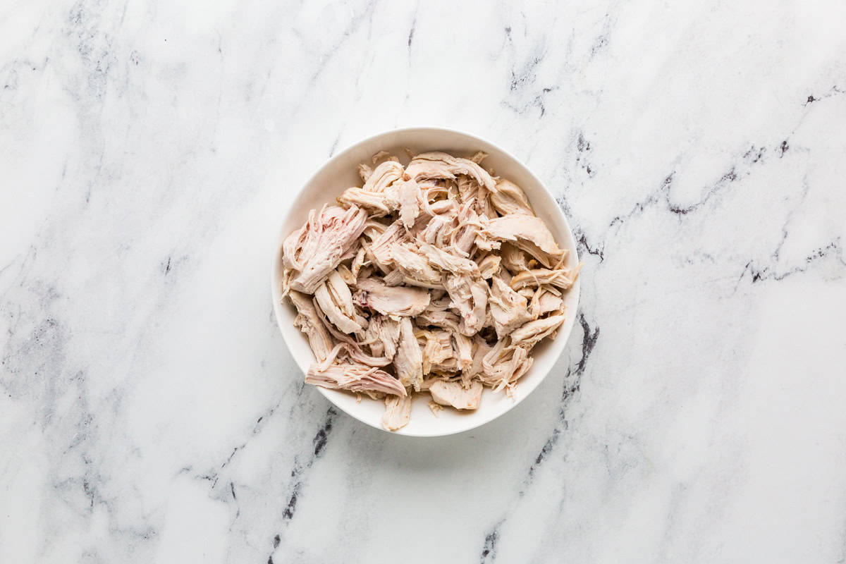 Bowl filled with cooked, shredded chicken.