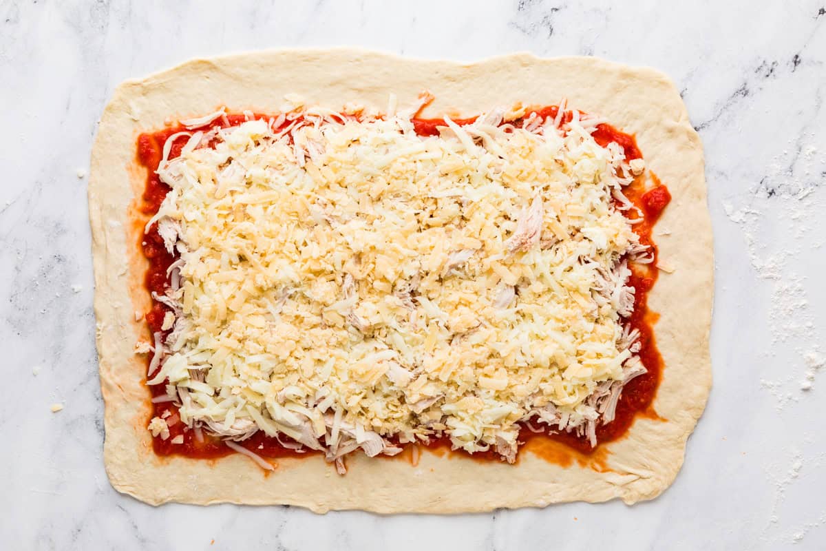 Rectangle of pizza dough, with layers of pizza sauce and cheese.