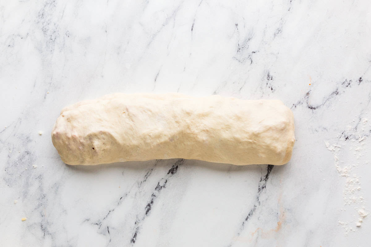 Log of pizza dough ready to be baked on a white counter.