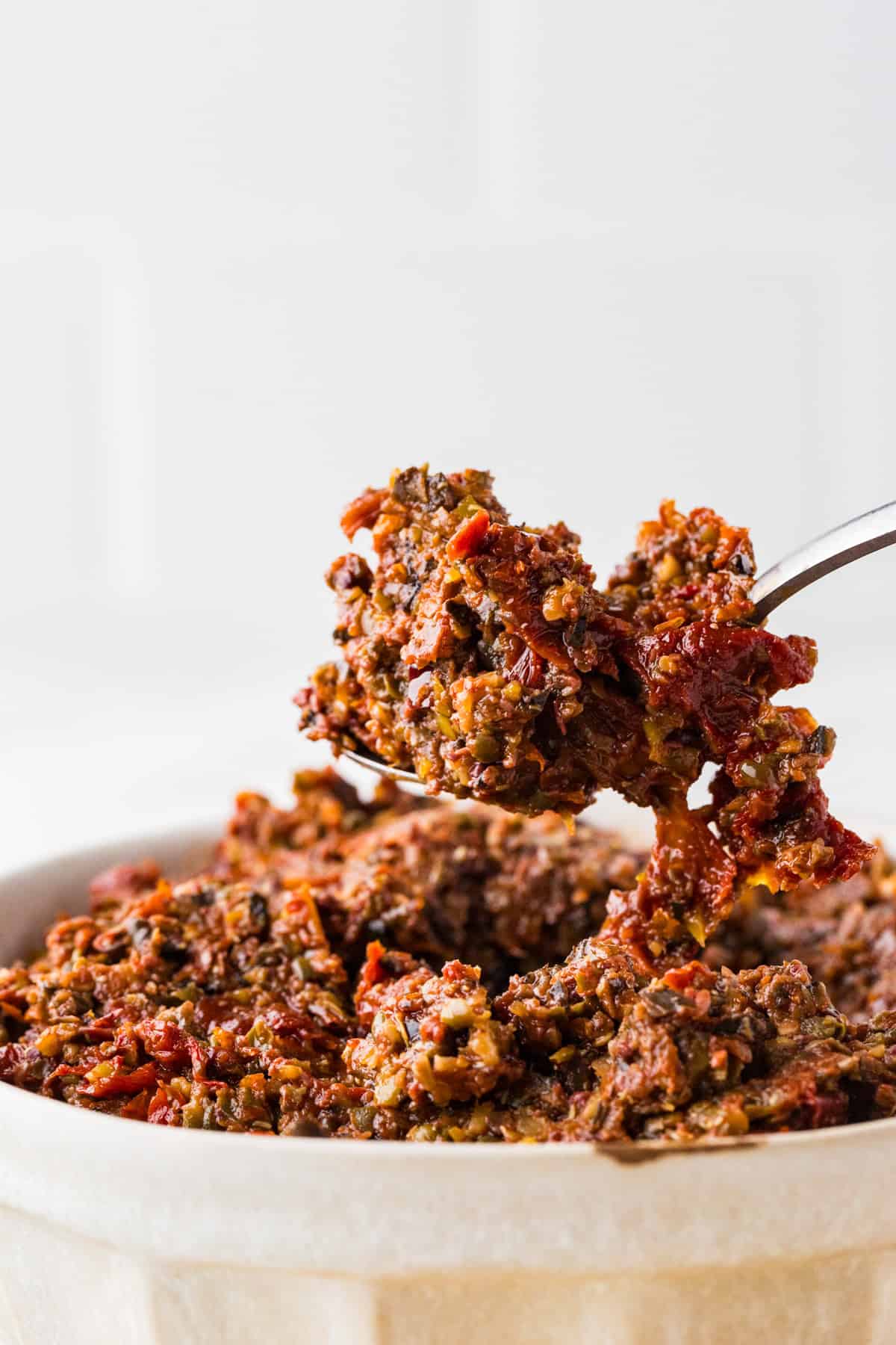 Spoon lifting a heaping spoonful of tapenade out of a bowl.