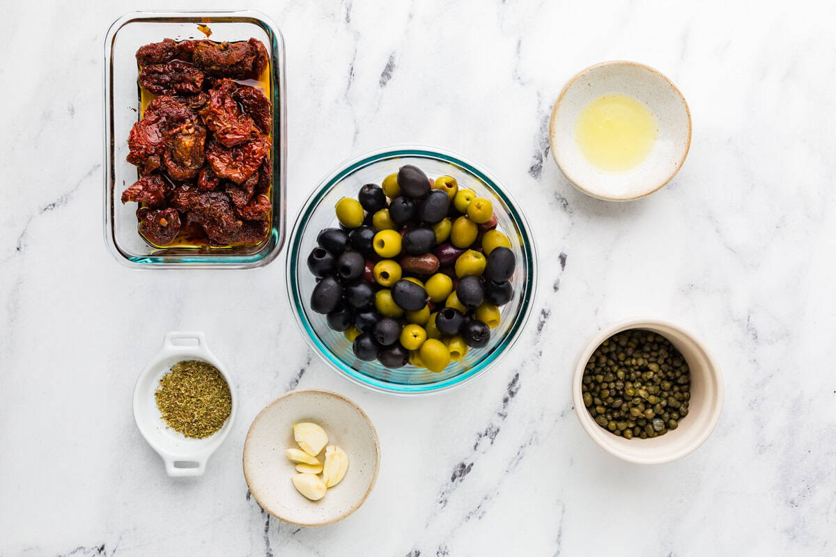 Ingredients for tapenade in individual bowls, sitting on a white counter.