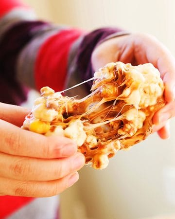 Close-up of a caramel popcorn ball being held with melted caramel stretching.