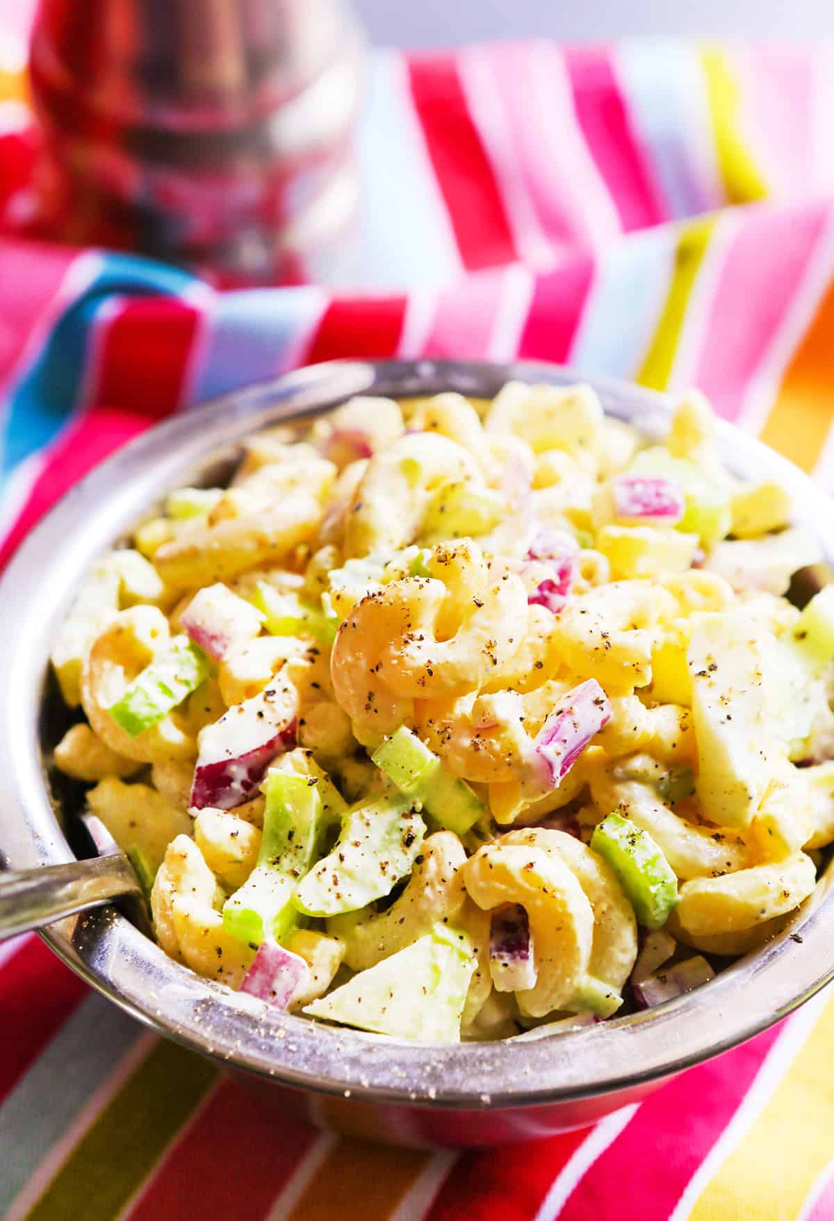 Classic creamy macaroni salad with celery, red onion, and herbs in a metal bowl.
