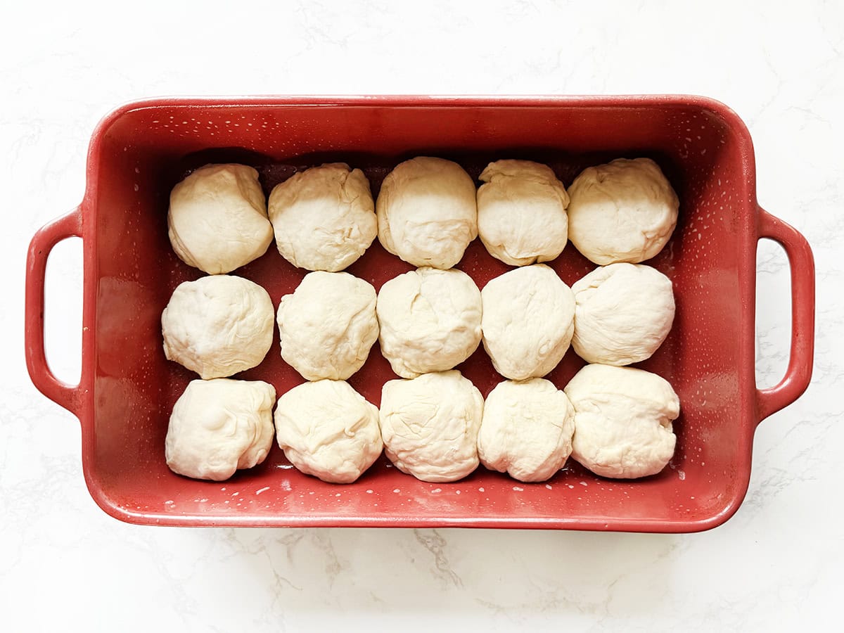 Dough balls arranged in a red baking dish for soft dinner rolls.