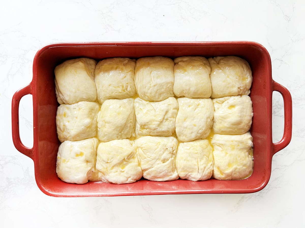 Soft dinner rolls in a red baking dish before baking.