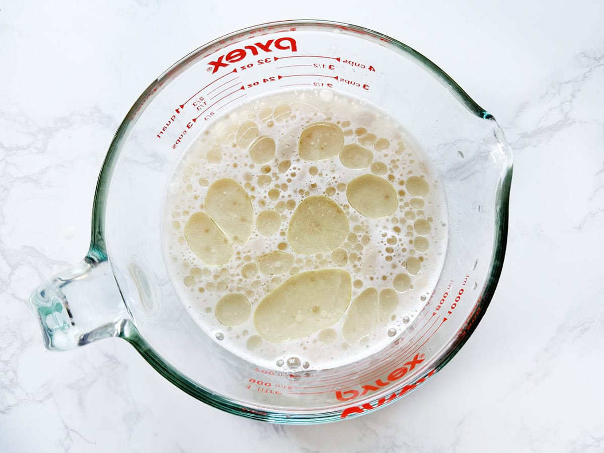 Creamy liquid with bubbles in a glass measuring cup on white surface.