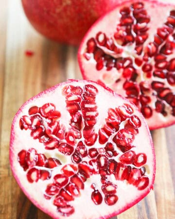 Close-up of a halved pomegranate showing its red seeds on a wooden surface.