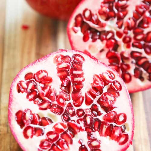 Close-up of a halved pomegranate showing its red seeds on a wooden surface.