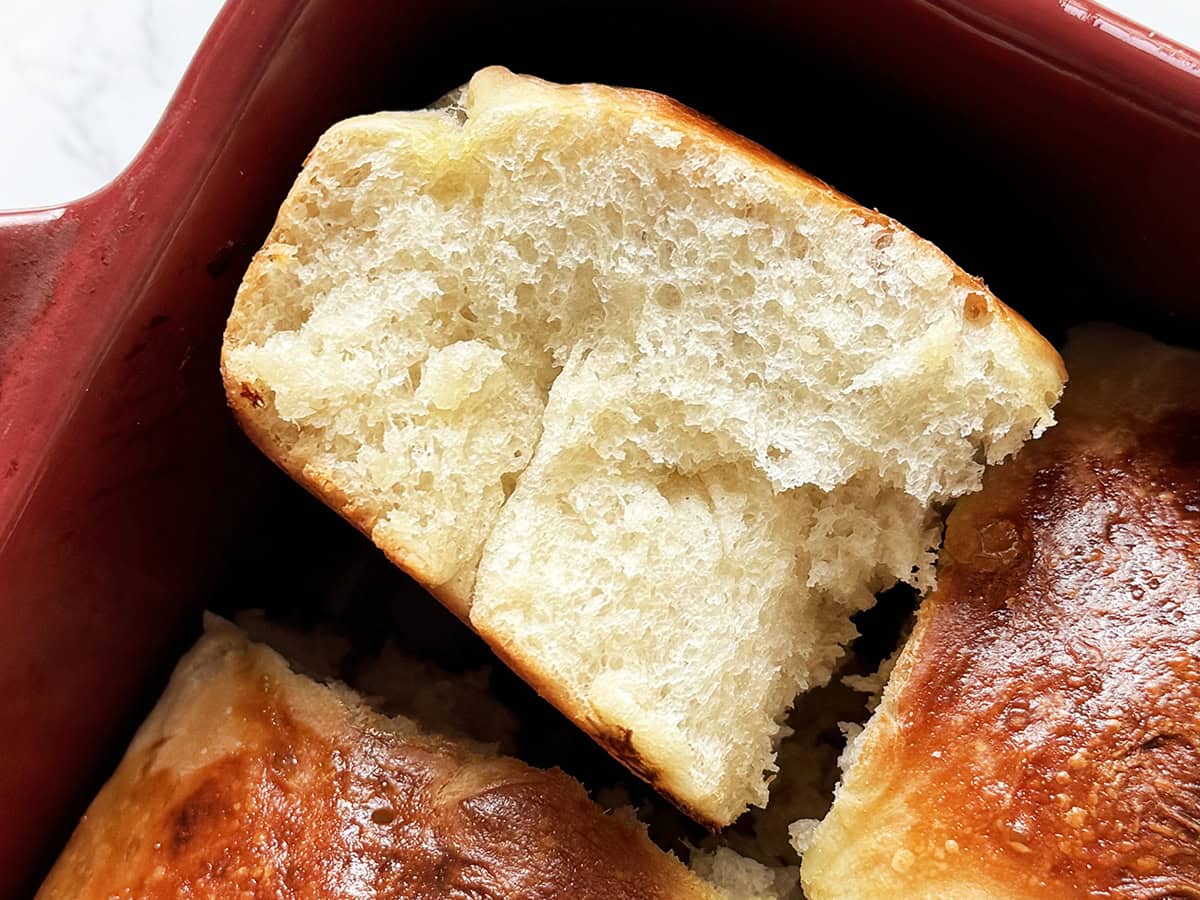 Soft, fluffy dinner roll with a golden crust in a red baking dish.