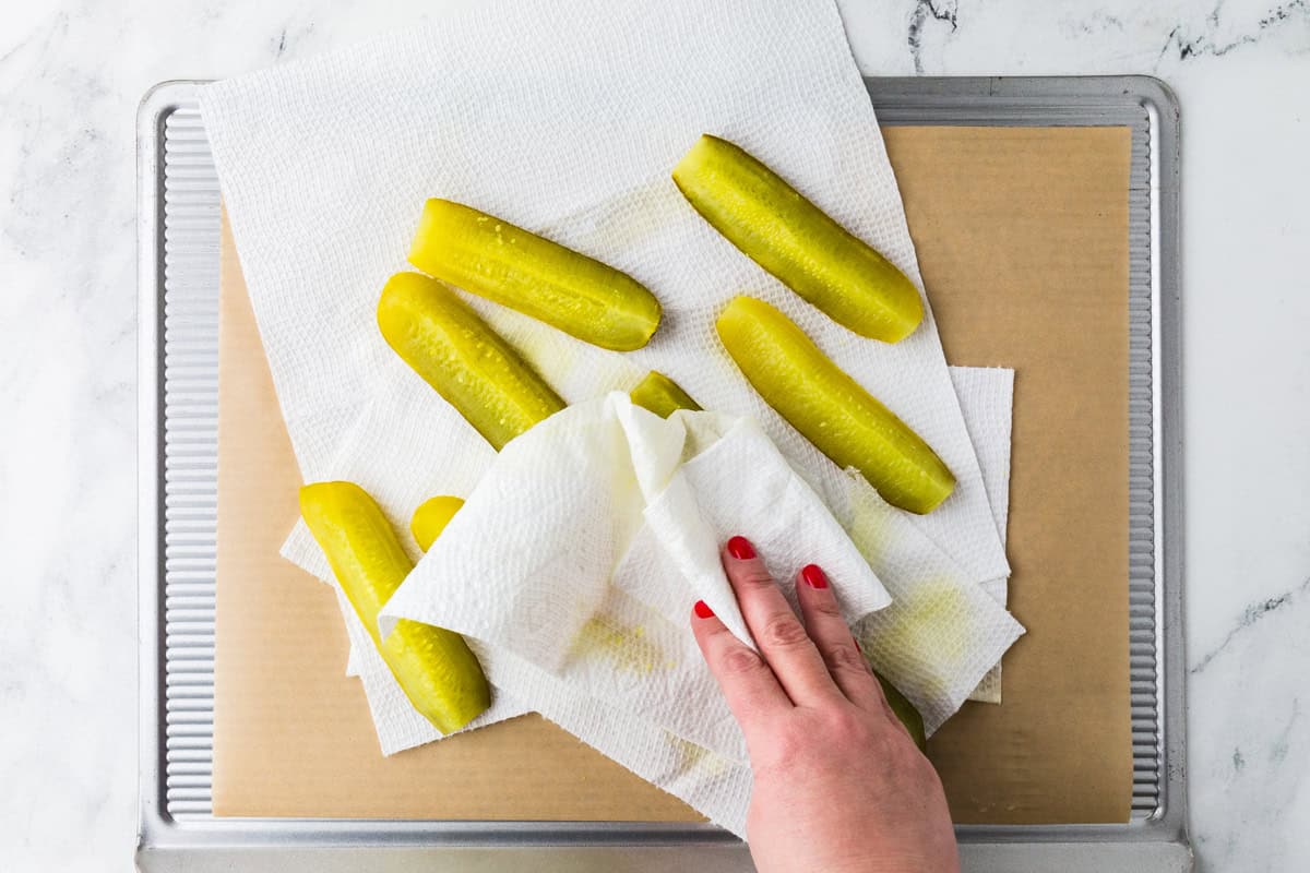 Hand pressing a paper towel onto dill pickle spears, removing juices.