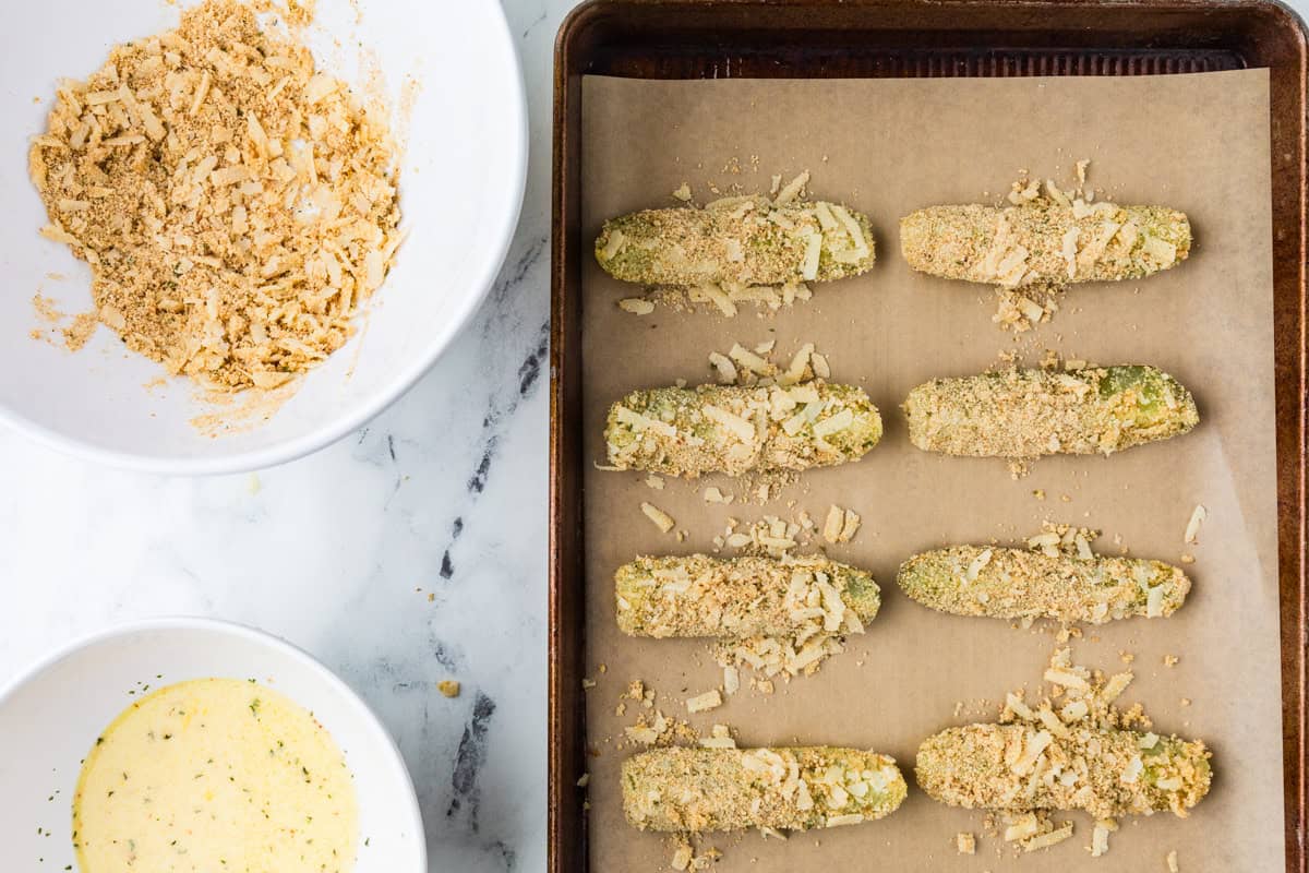 Pickle fries lined up on a baking sheet, ready to go into the oven.